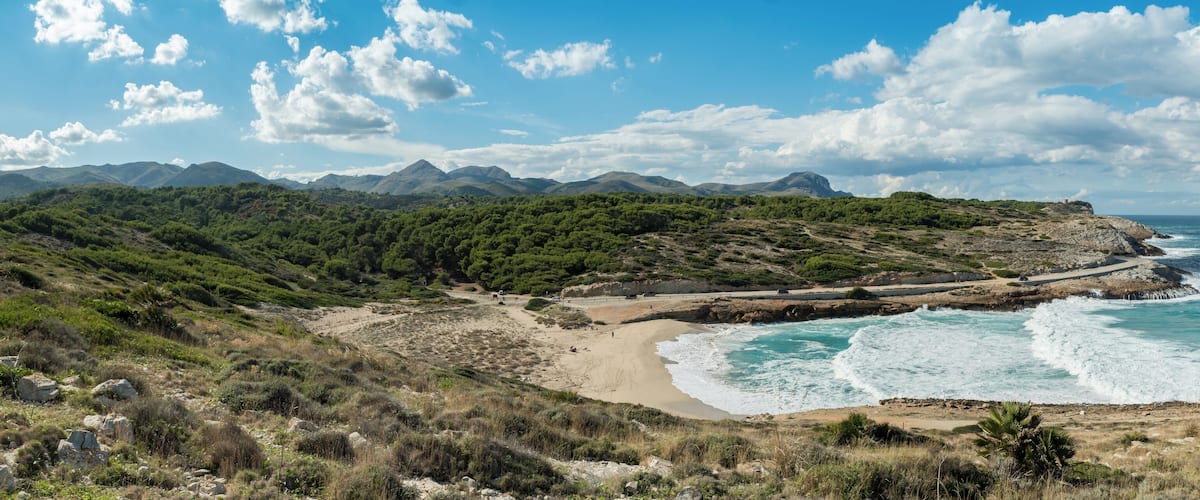 A coastal landscape with a sandy beach, rocky cliffs, and a mountainous backdrop.