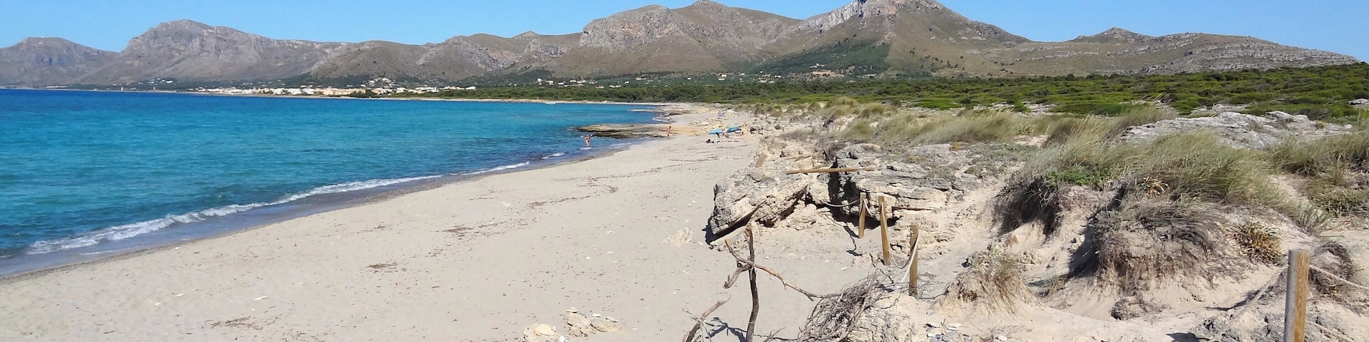 Una playa con agua azul cristalina, orilla arenosa y montañas al fondo.