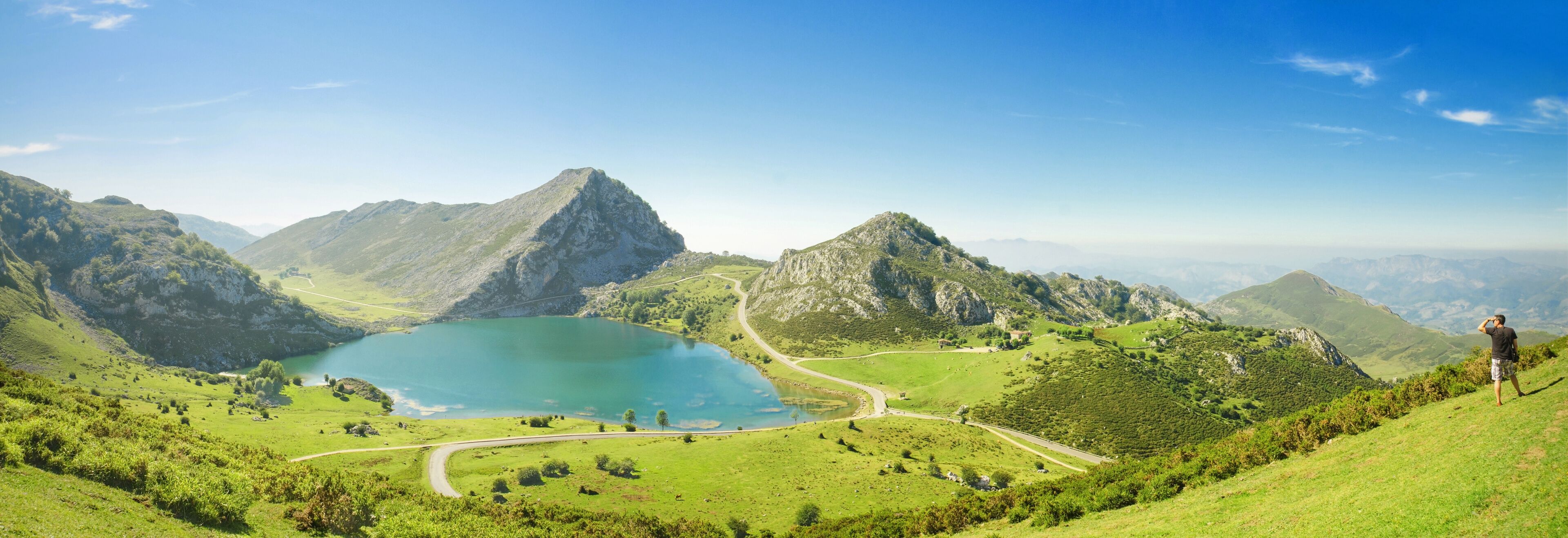 Eine Berglandschaft mit einem See, gewundenen Straßen und einer Person, die auf einem Hügel steht.