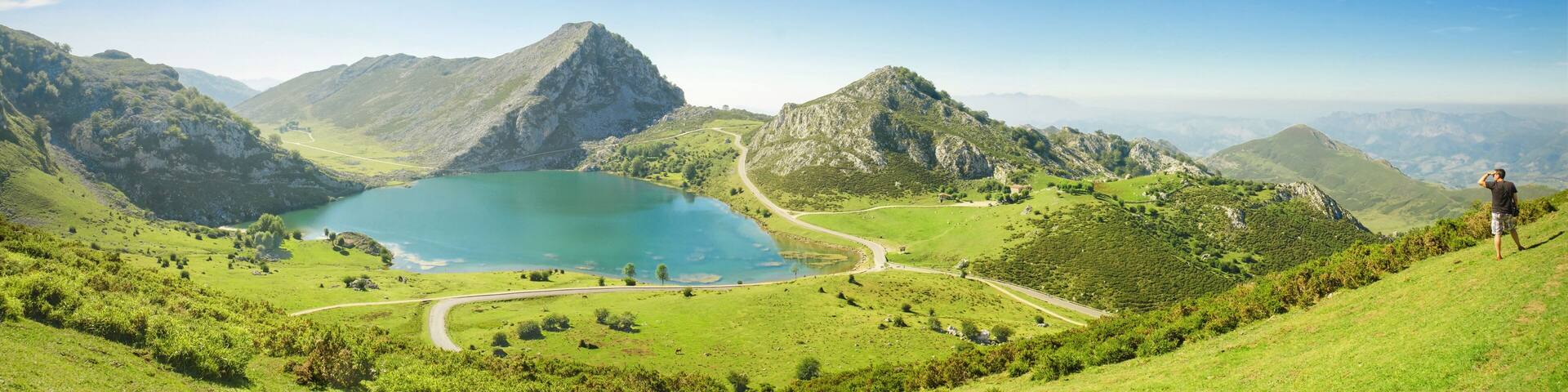 A mountainous landscape with a lake, winding roads, and a person standing on a hill.