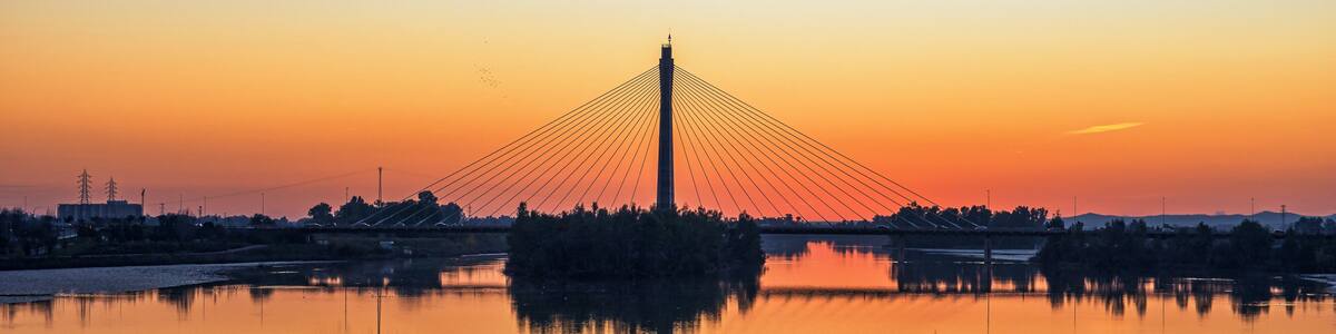 A cable-stayed bridge at sunset with a calm river reflecting its structure.