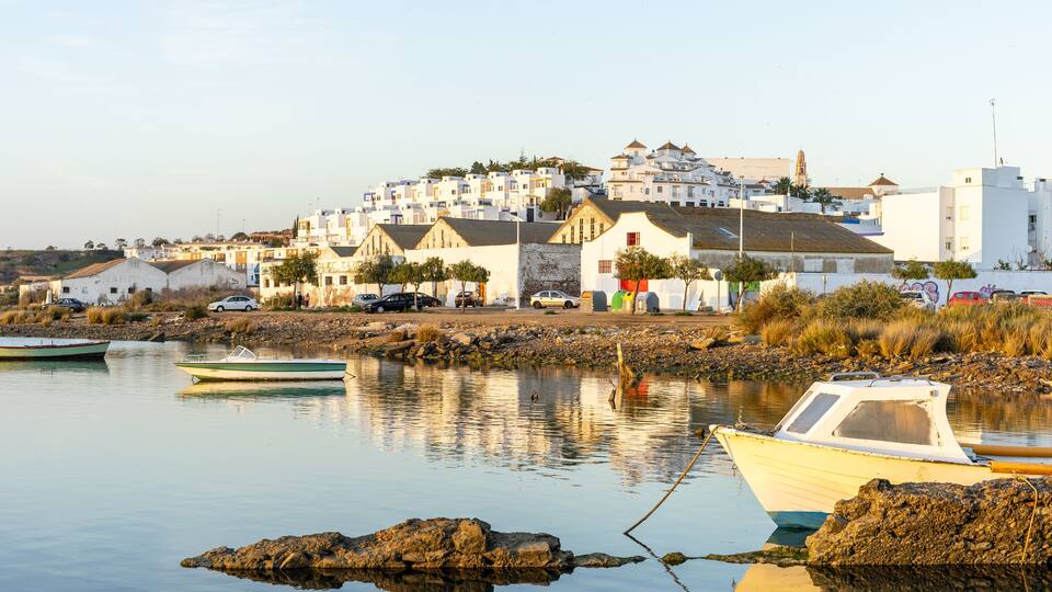 A coastal town with white buildings, a rocky shoreline, and boats in the water.