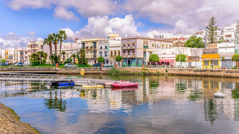 A waterfront with colorful buildings, a calm river, and a bridge.