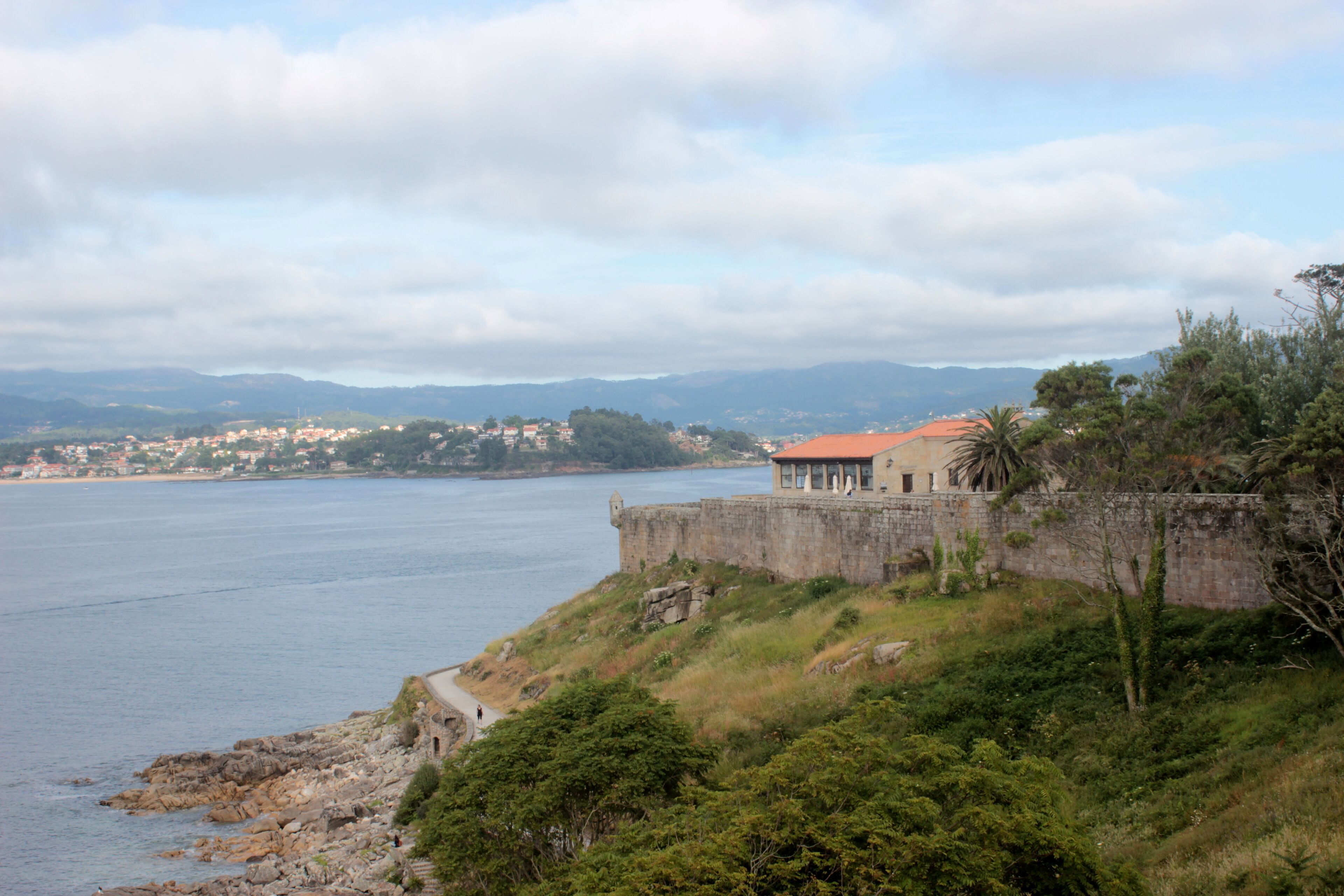 A coastal town with a prominent stone fortification and a red-roofed building overlooking the sea.