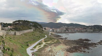 A coastal city with a historic stone wall, a winding path, and a view of the sea and distant mountains.