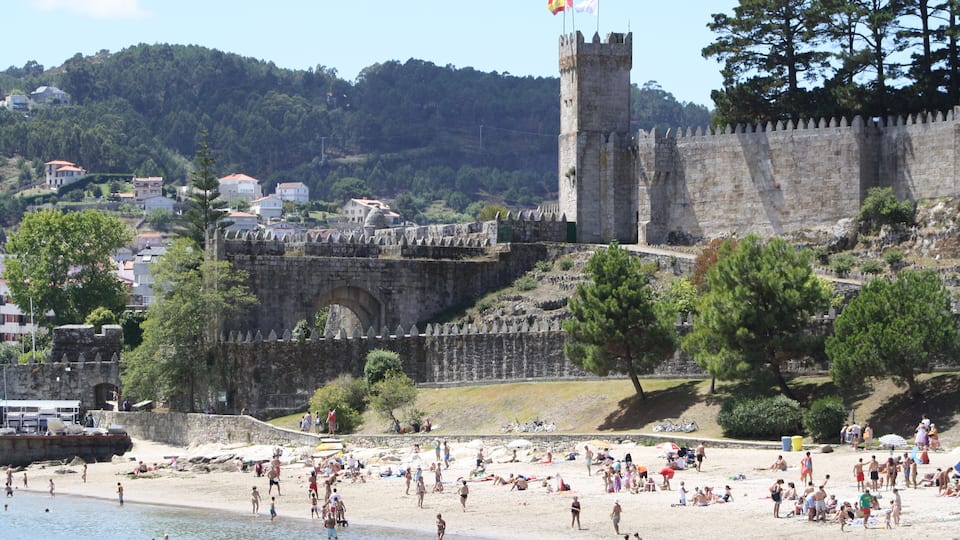 Una playa con gente, un castillo y una bandera.