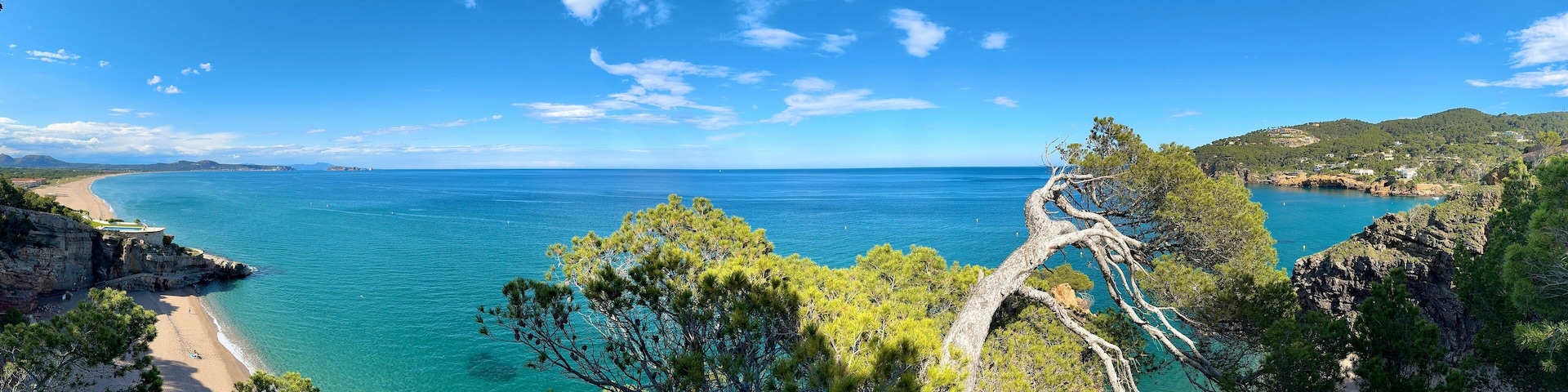 A coastal landscape with clear turquoise waters, a sandy beach, and rocky cliffs with pine trees.