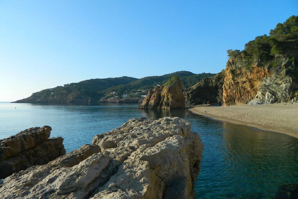 Eine Küstenlandschaft mit klarem, blauem Wasser, Felsformationen und einem Sandstrand.