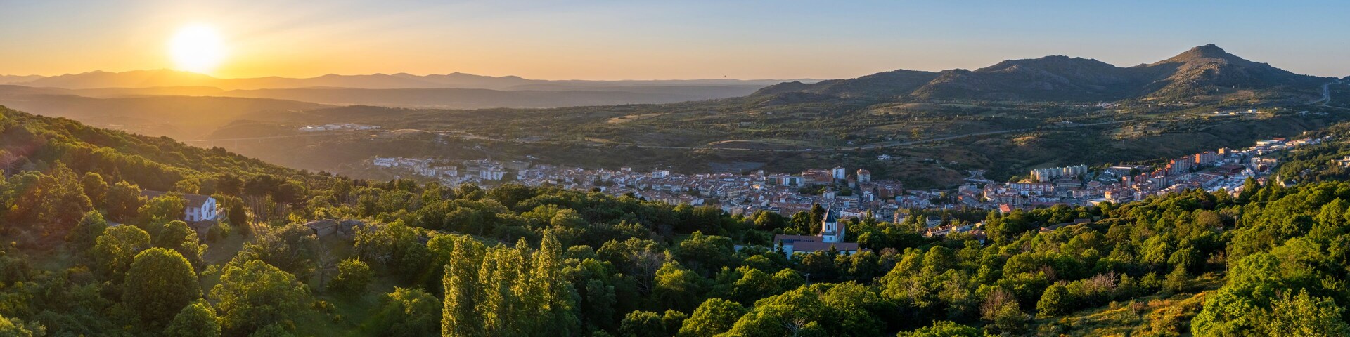 A city nestled in a valley with mountains in the background and a clear sky.