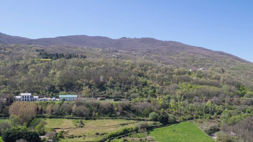 A rural landscape with a hill, green fields, a few buildings, and a clear sky.