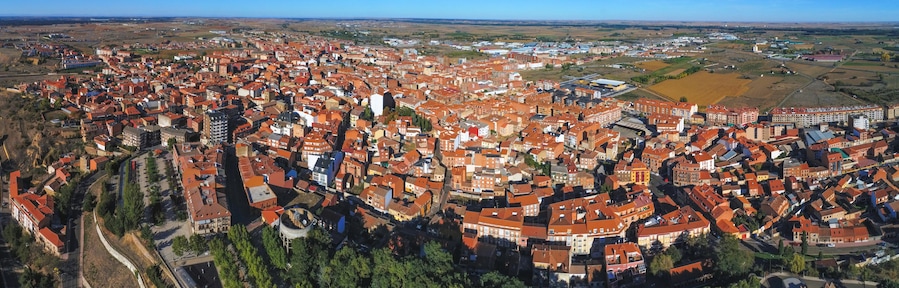 Une zone urbaine densément peuplée, avec des bâtiments aux toits rouges, entourée de vastes champs et de collines lointaines.