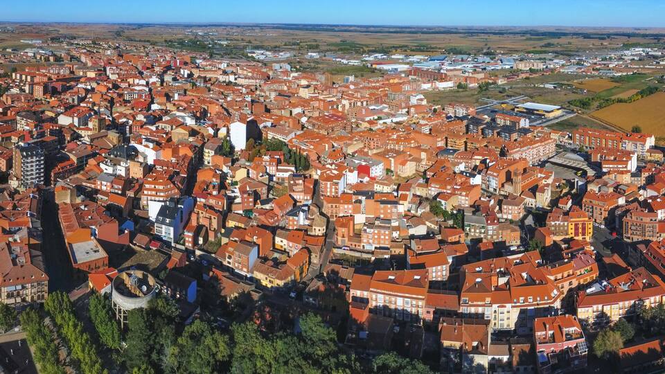 A densely packed urban area with red-roofed buildings, surrounded by open fields and distant hills.
