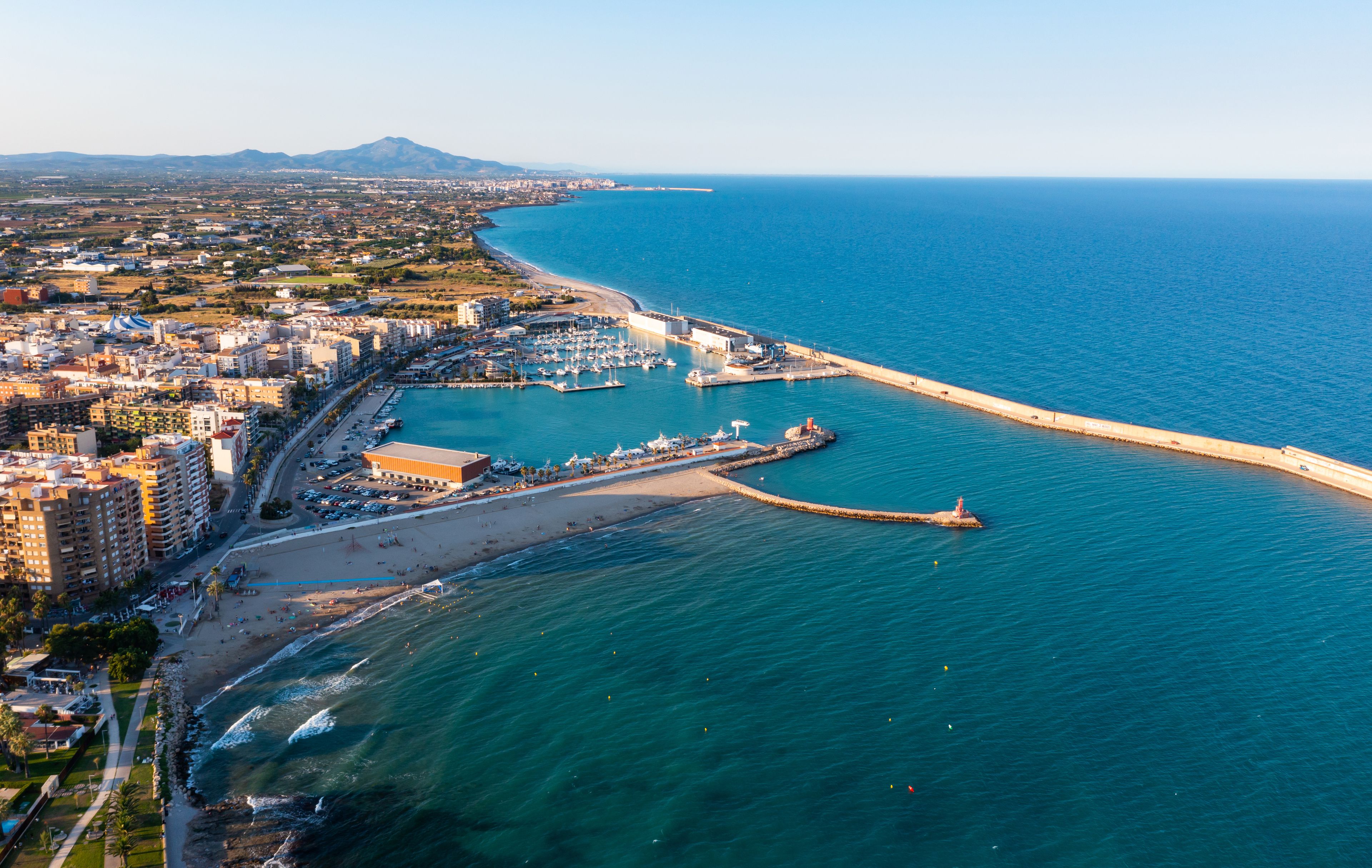 Una ciudad costera con un puerto deportivo, playa y un muelle largo que se adentra en el mar.
