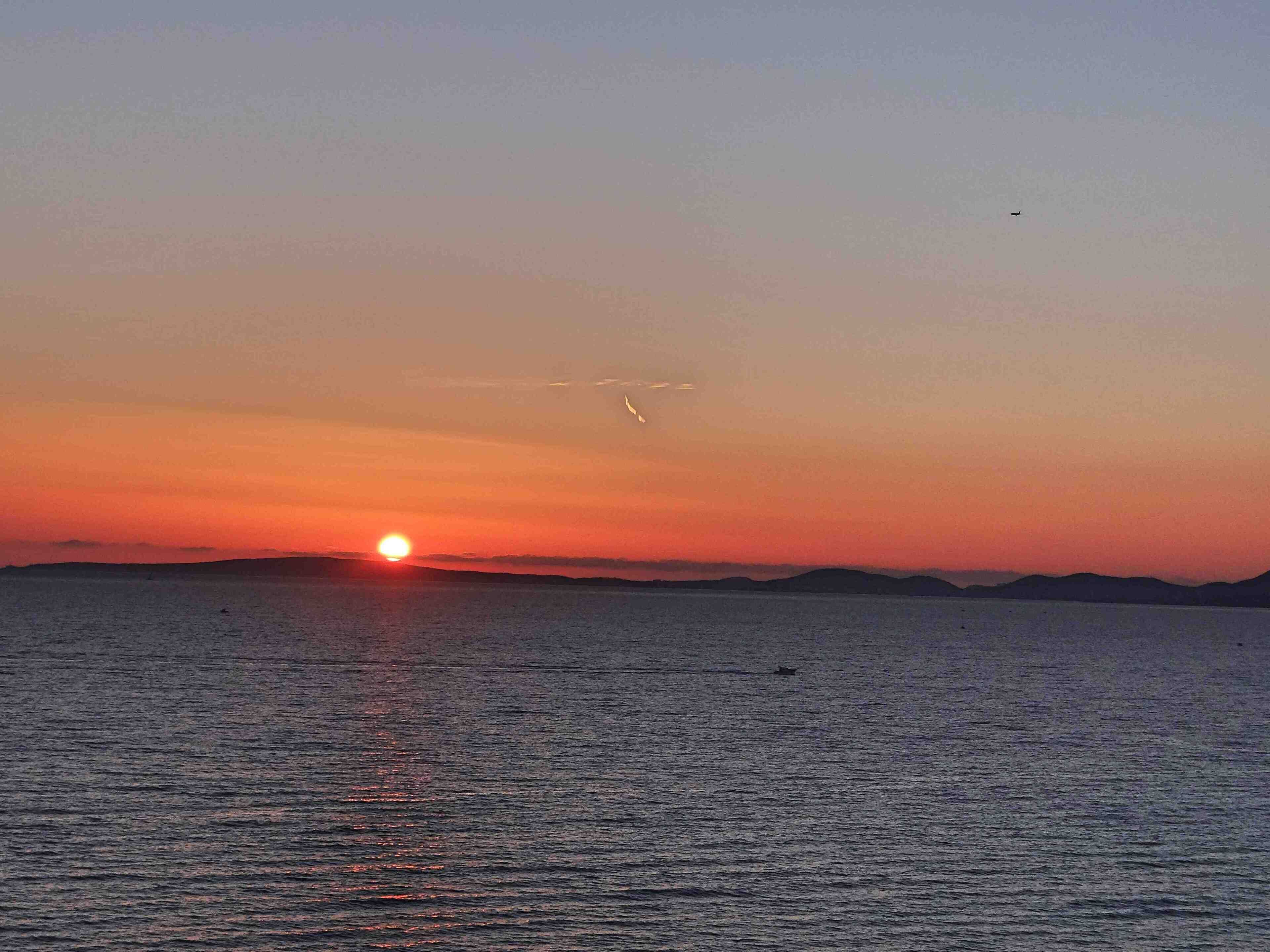 Un atardecer sobre un mar tranquilo con el silueta de colinas lejanas.