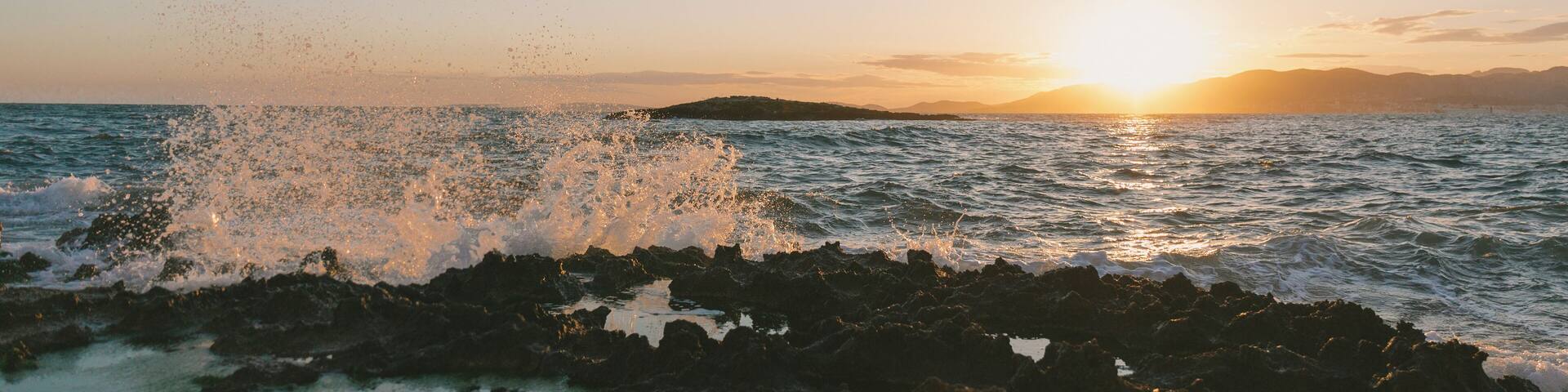 A sunset over a rocky coastline with waves crashing against the rocks.