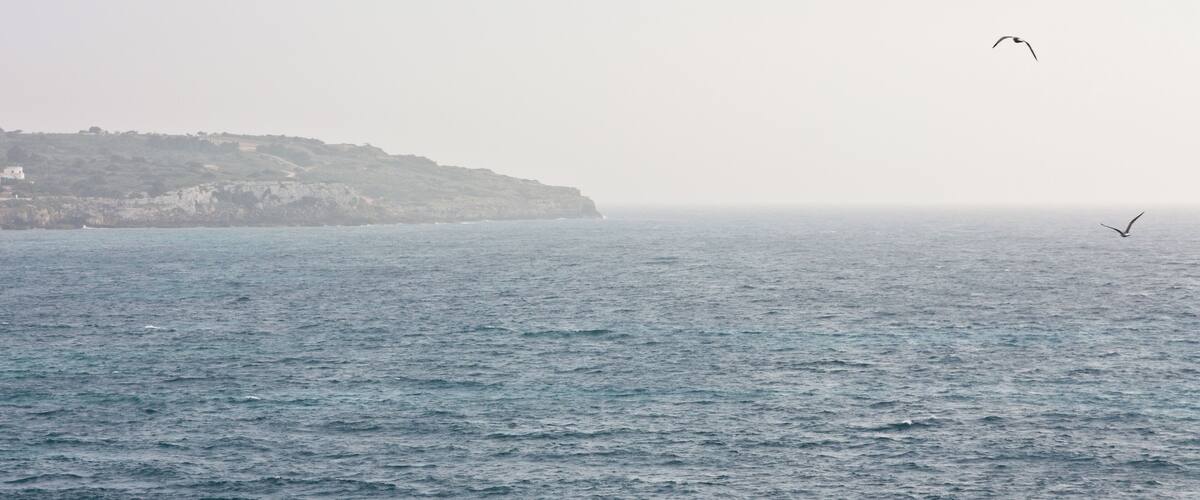 A coastal landscape with a rocky cliff and calm sea.