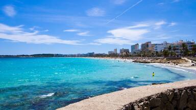 Un paisaje urbano costero con cielo azul despejado, mar turquesa y una playa de arena.