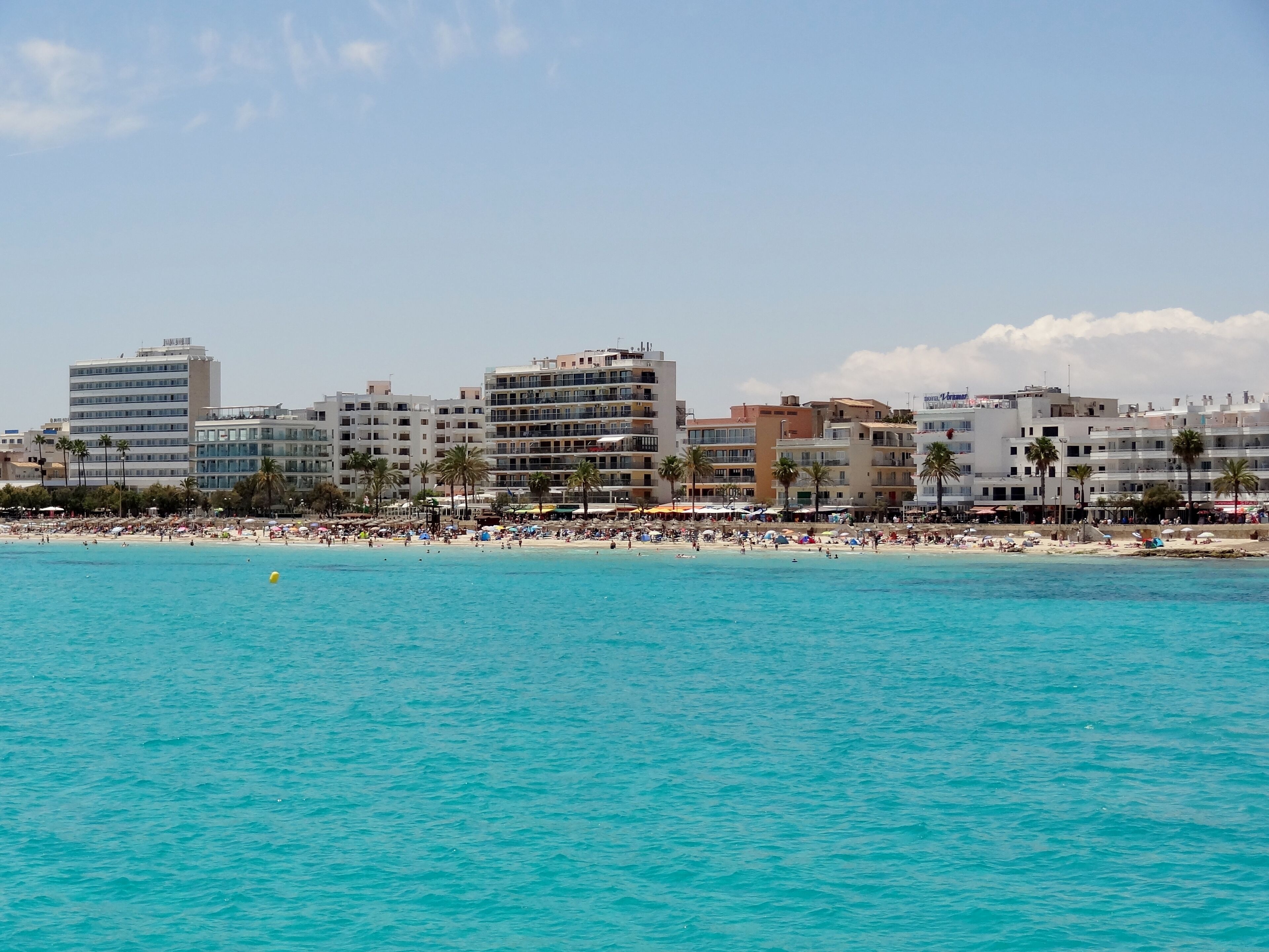 A beach with turquoise water, palm trees, and a row of buildings in the background.