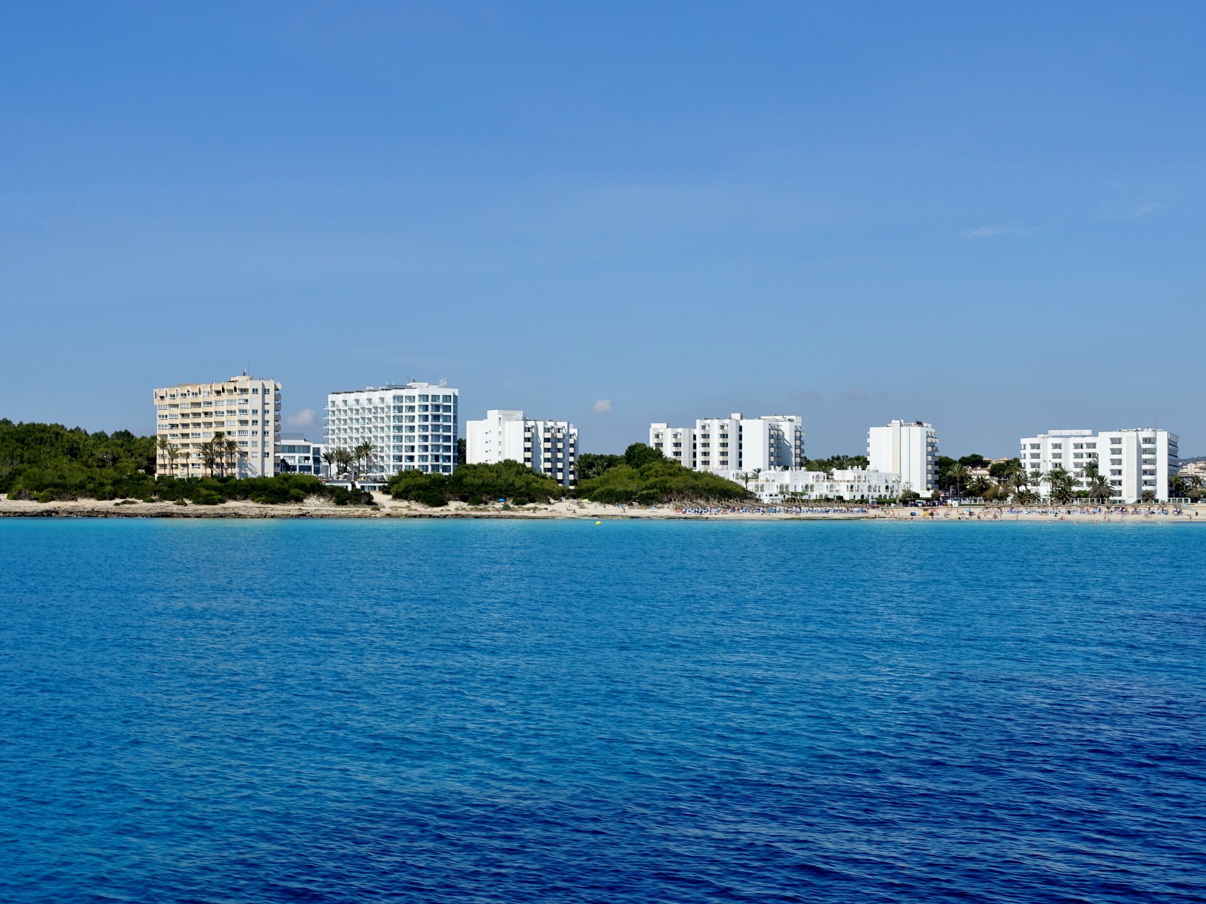 A coastal cityscape with a beach and several white buildings along the shoreline.
