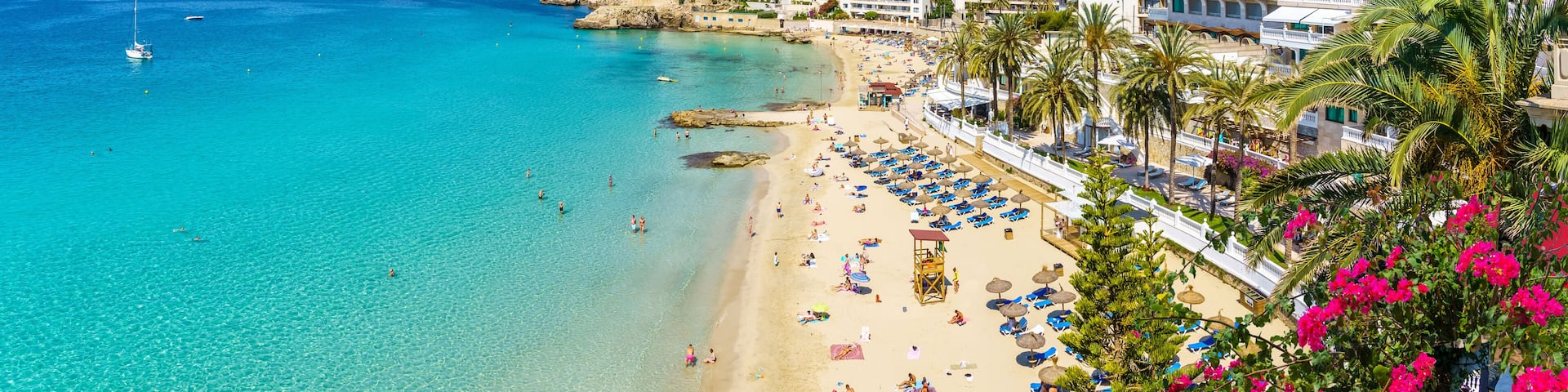A coastal cityscape with a beach, clear turquoise waters, and a mix of residential and hotel buildings.