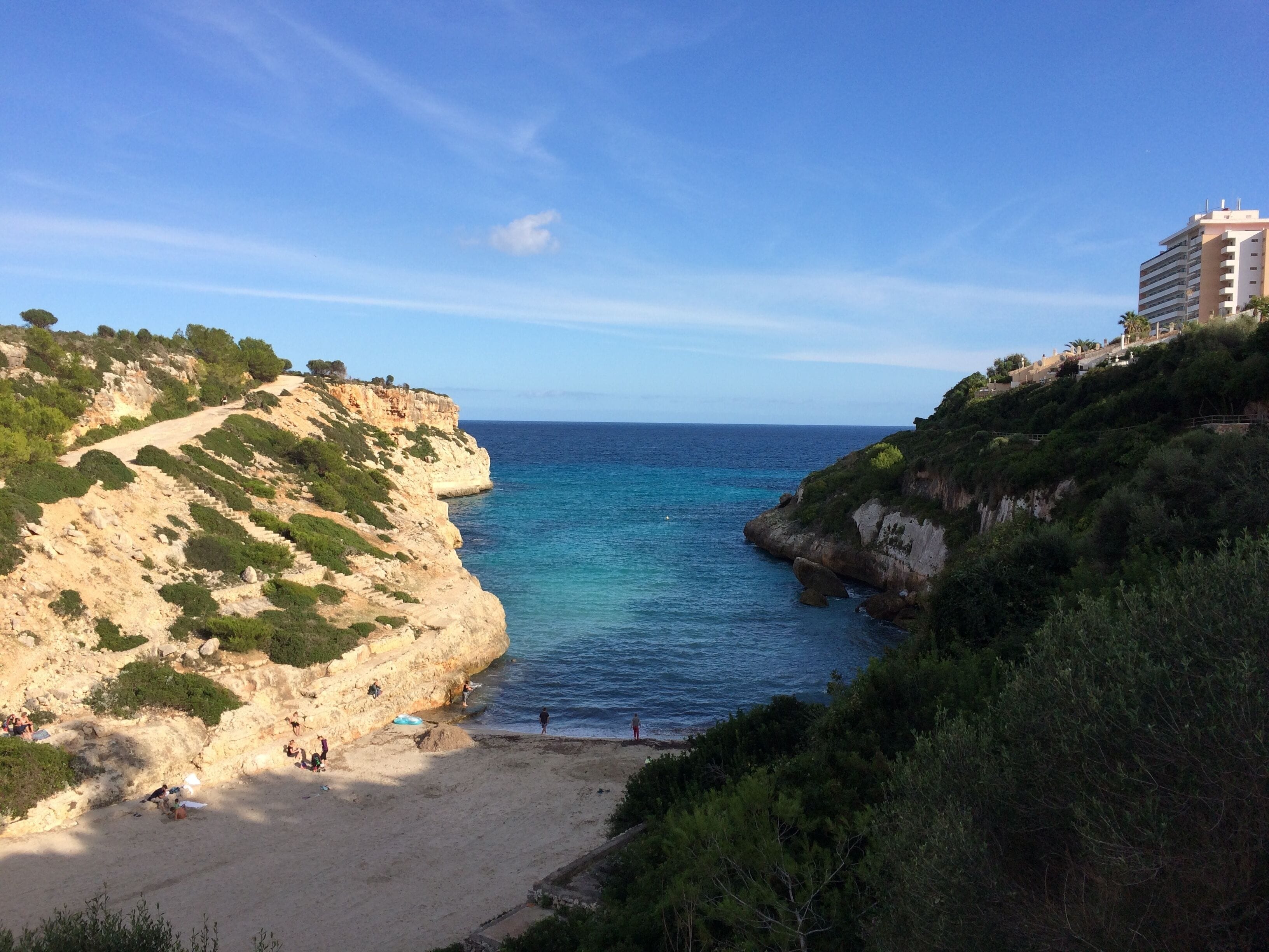 A coastal landscape with a sandy beach, rocky cliffs, and a clear blue sea.