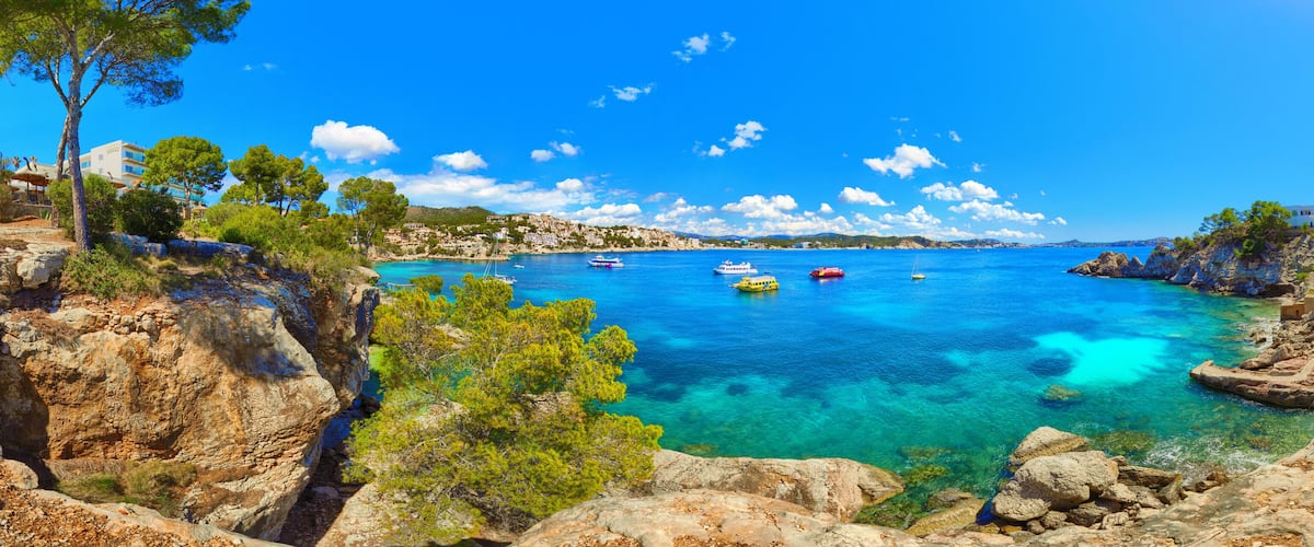 A coastal landscape with clear blue waters, rocky cliffs, and boats.