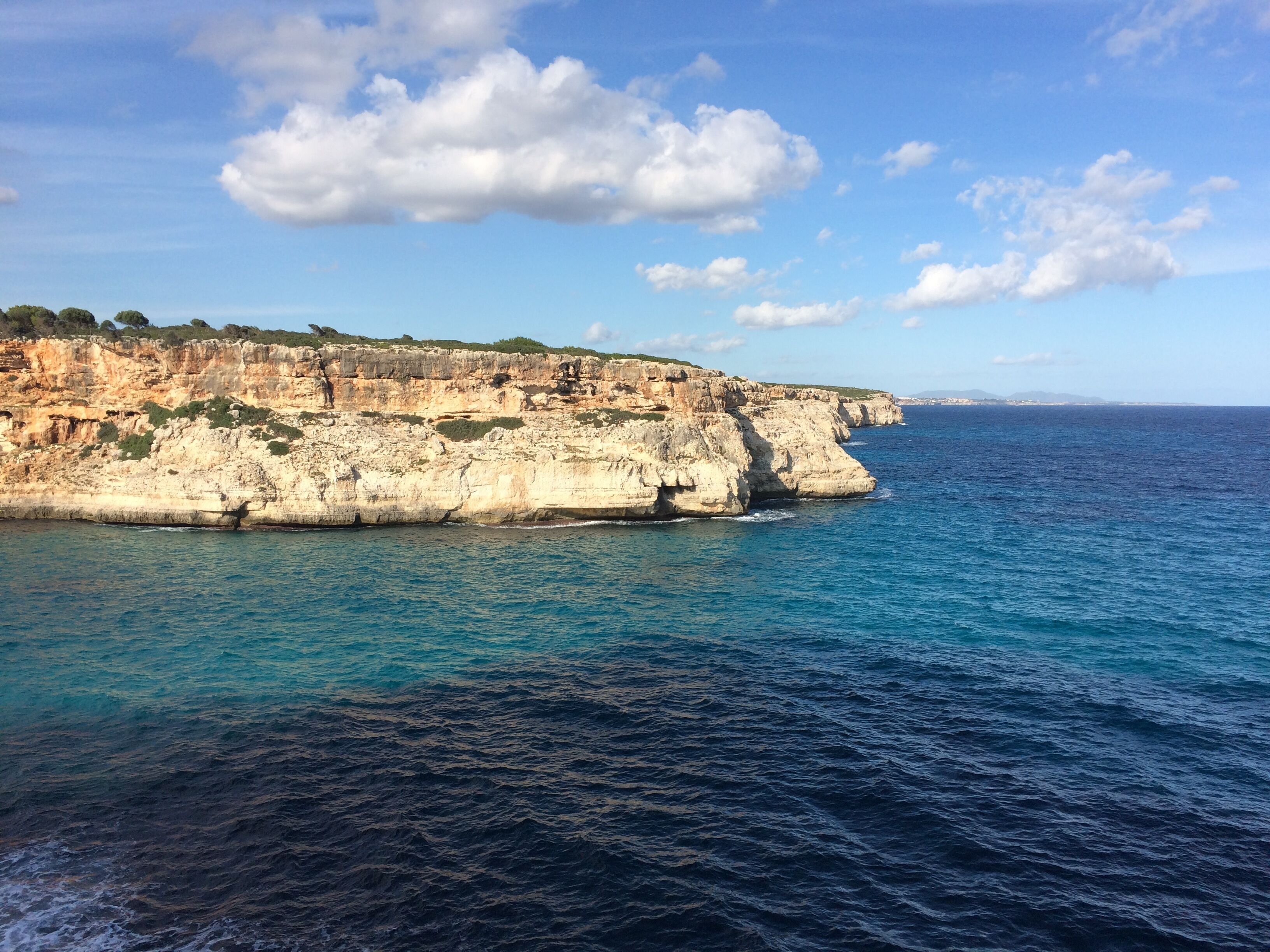 A coastal cliff with a clear blue sea and a partly cloudy sky.