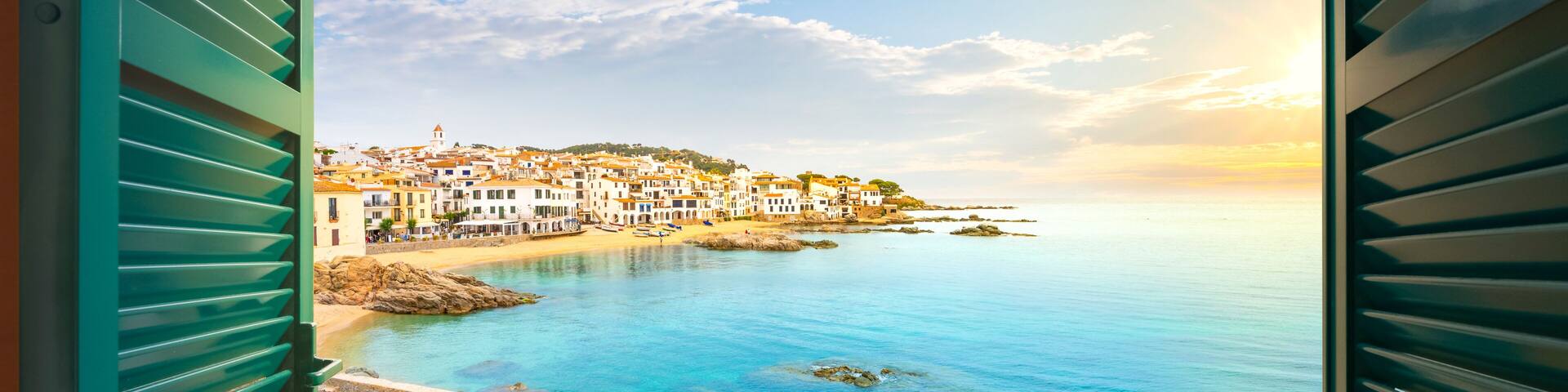 A coastal town with colorful flowers in the foreground, clear blue waters, and buildings on a hillside.