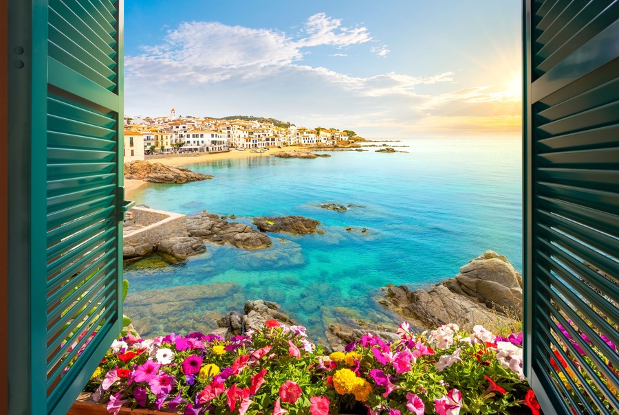 Un pueblo costero con flores coloridas en primer plano, aguas azules cristalinas y edificios en una ladera.