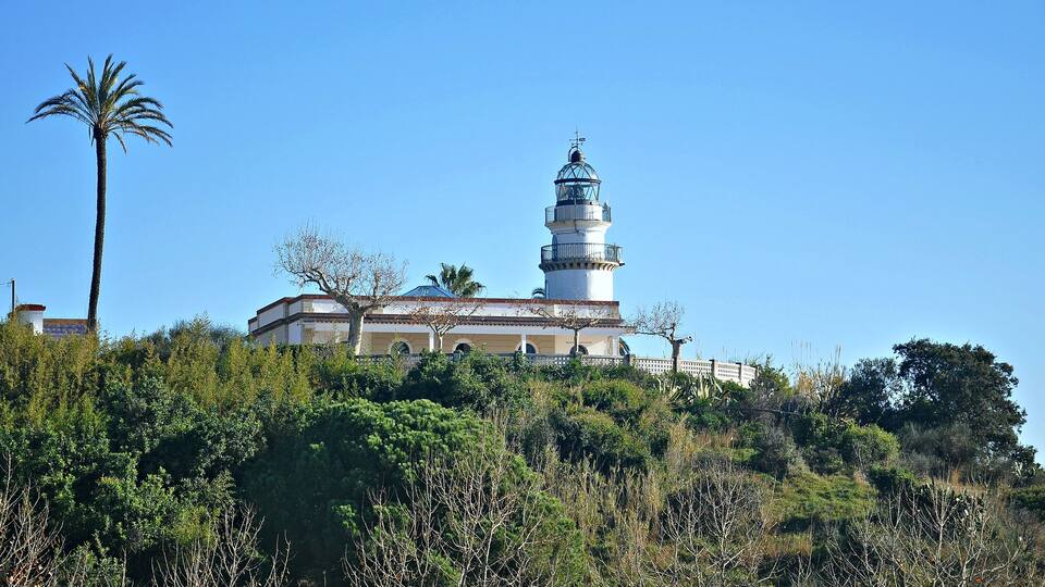 A lighthouse on a hill with surrounding greenery and a clear blue sky.