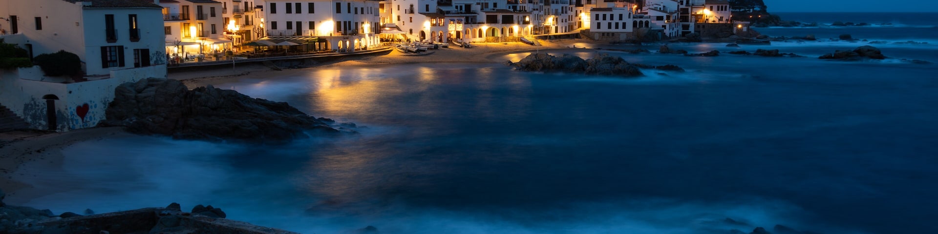 Night view of a mediterranean coastal town, Calella de Palafrugell, Spain, with illuminated buildings reflected on the sea