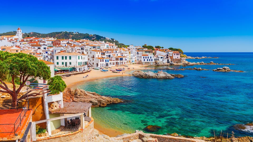A coastal town with white buildings, a beach, and clear blue waters.