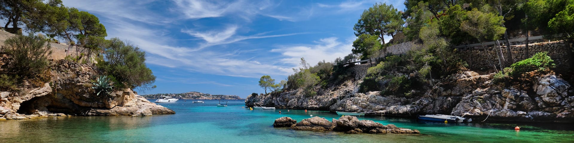 A coastal landscape with clear turquoise waters, rocky cliffs, and boats anchored near the shore.