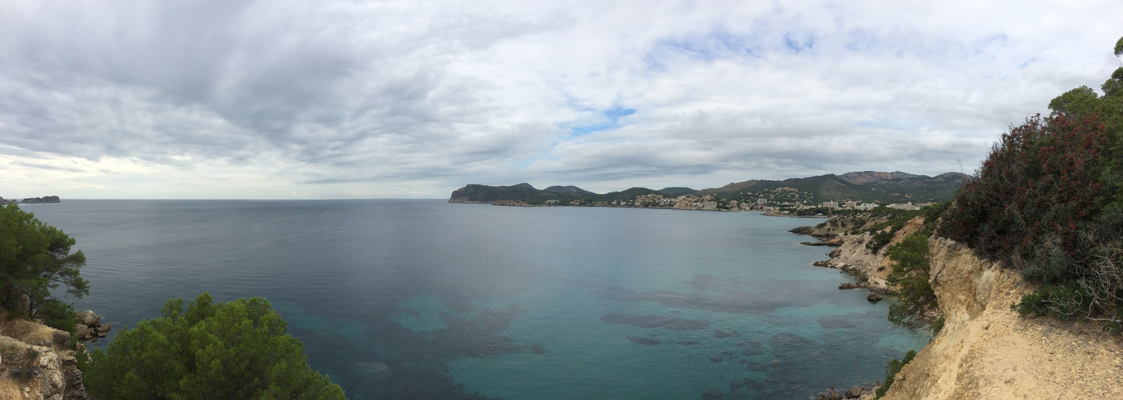 A coastal landscape with clear turquoise waters, rocky cliffs, and a distant cityscape.