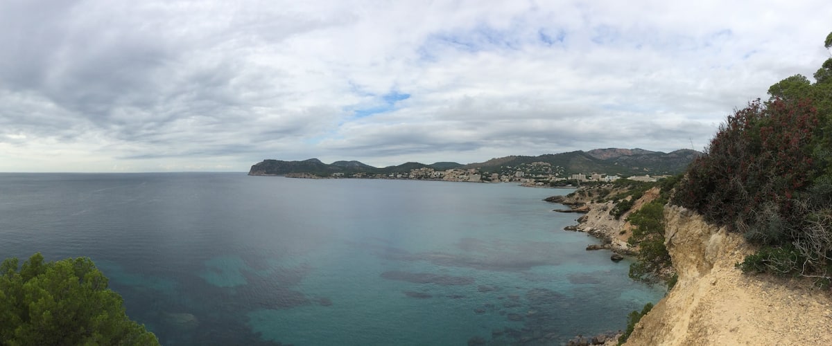 A coastal landscape with clear turquoise waters, rocky cliffs, and a distant cityscape.