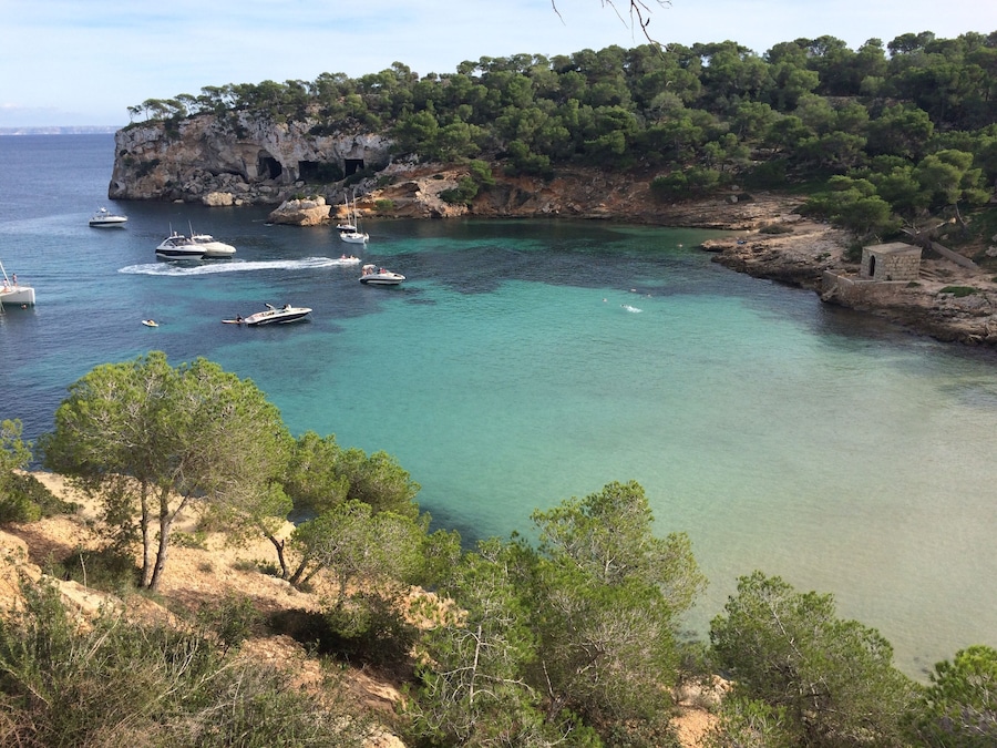 Un paisaje costero con aguas turquesas cristalinas, embarcaciones y un acantilado rocoso con árboles.
