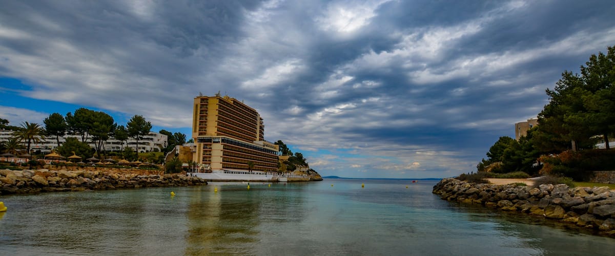 A coastal scene with a hotel, calm water, and rocky shorelines.