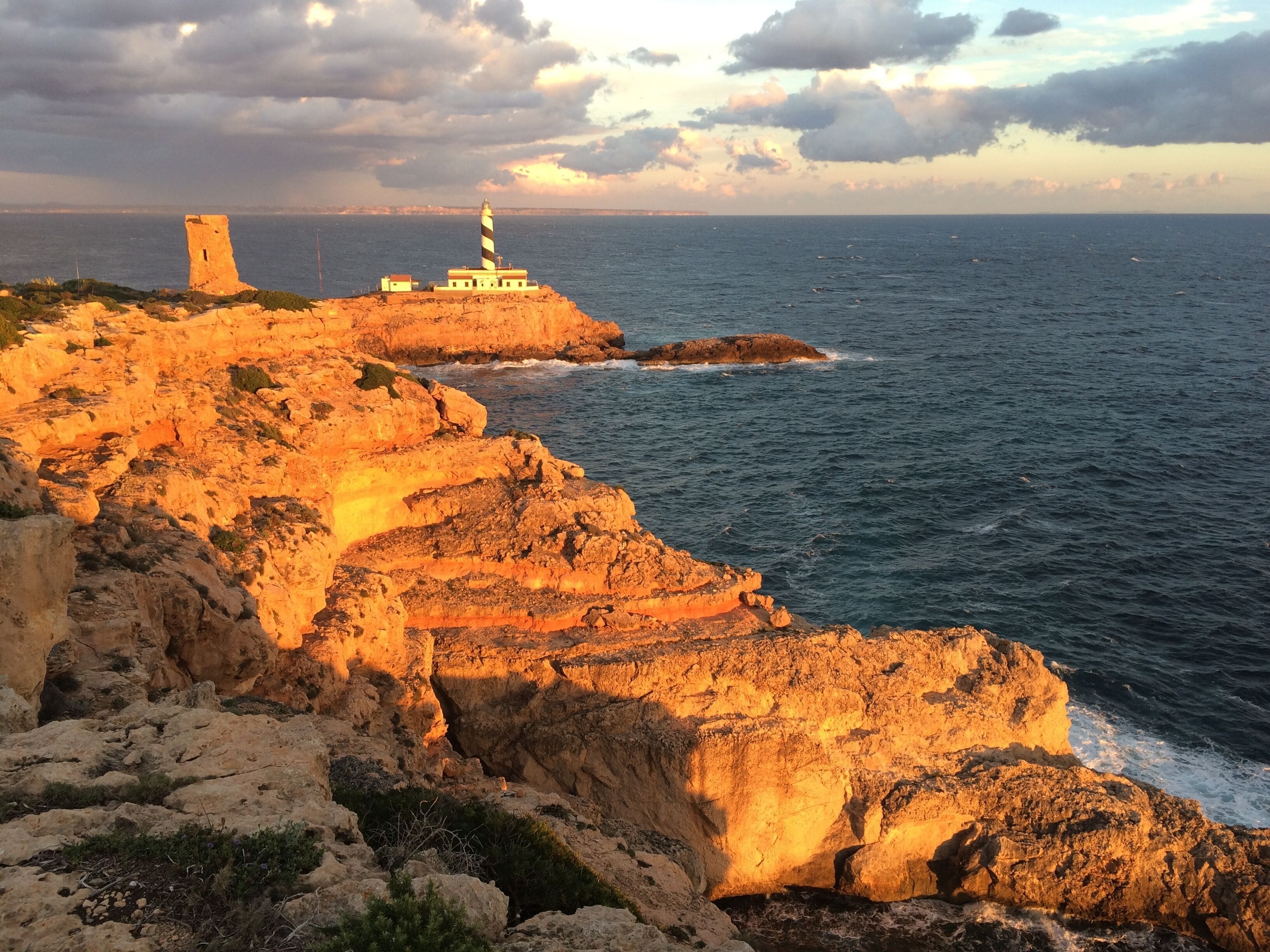 A coastal landscape with a lighthouse and a tower on a rocky cliff overlooking the sea.