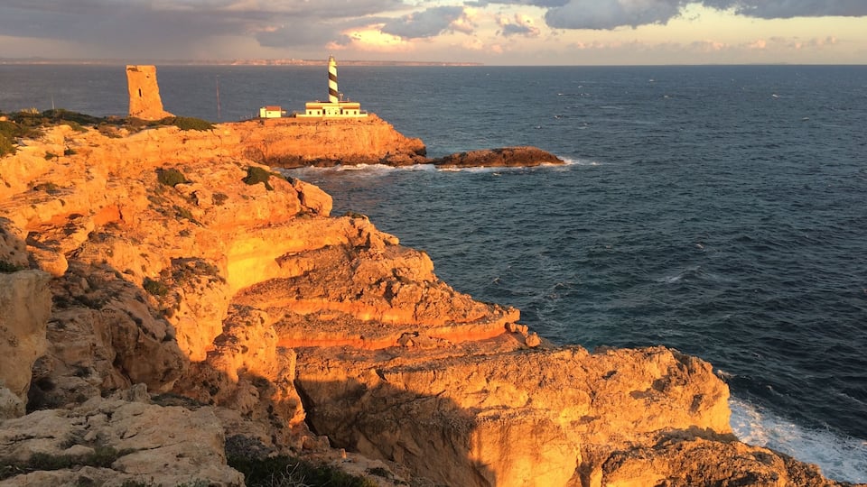 A coastal landscape with a lighthouse and a tower on a rocky cliff overlooking the sea.