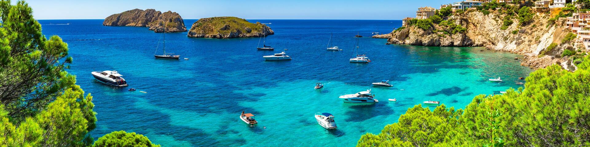 A coastal scene with clear turquoise waters, boats, rocky outcrops, and lush greenery.