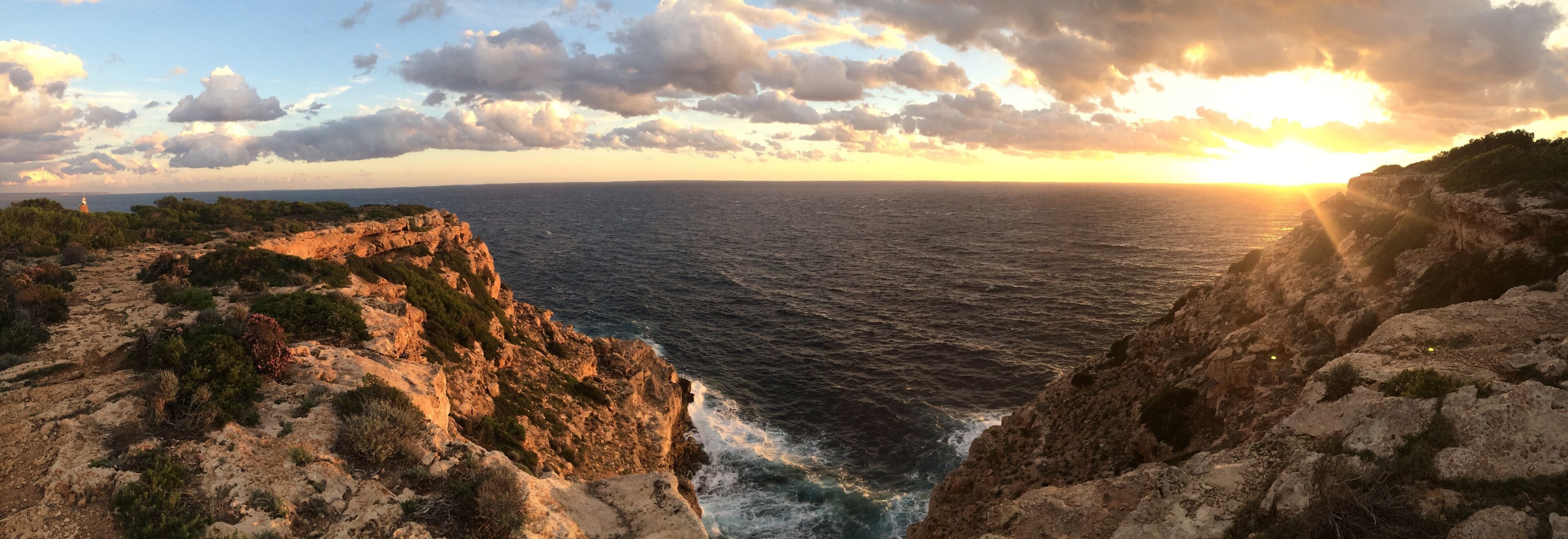A coastal landscape with rocky cliffs, a sea, and a sunset.