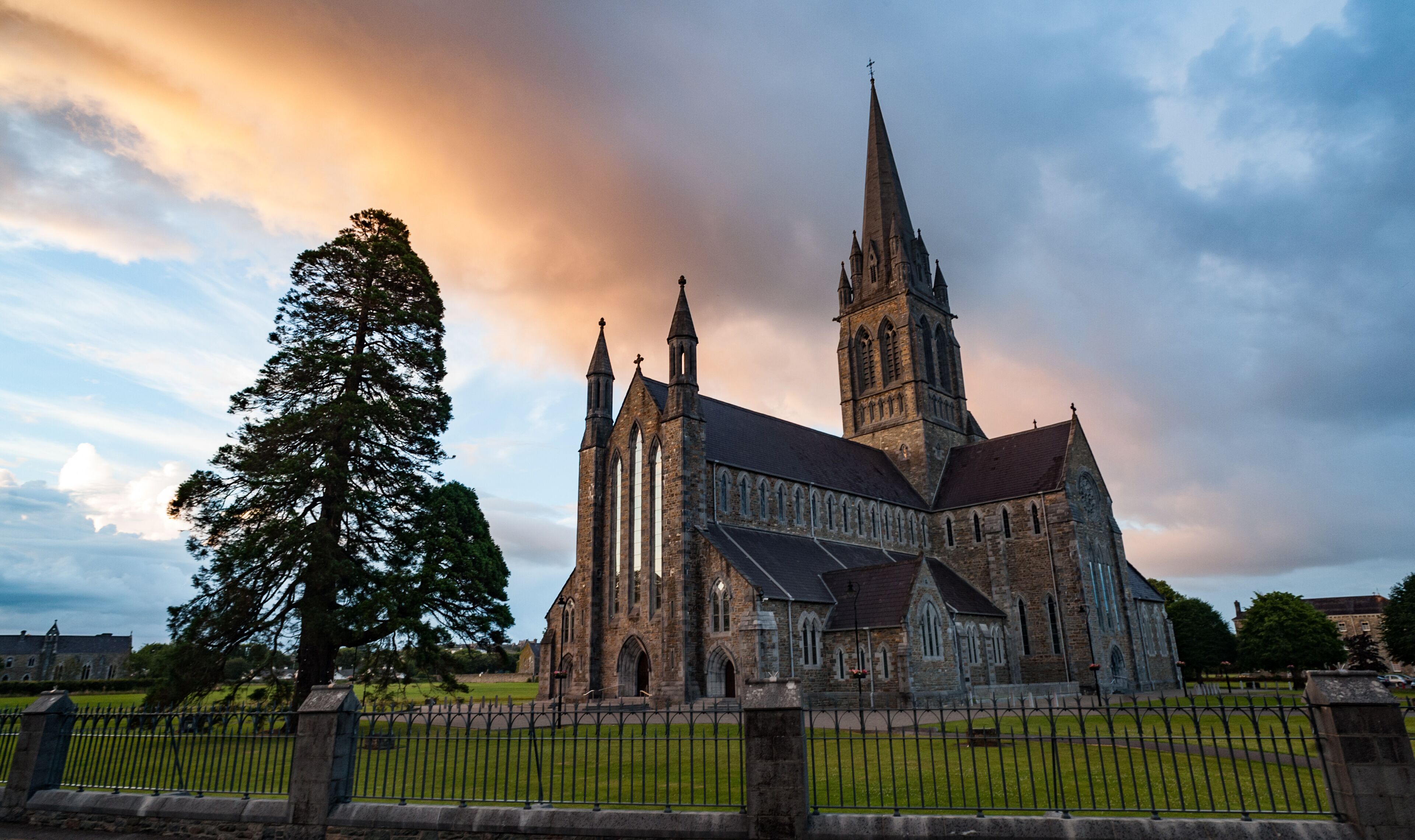 A historic church with a tall spire and a large tree in the foreground.