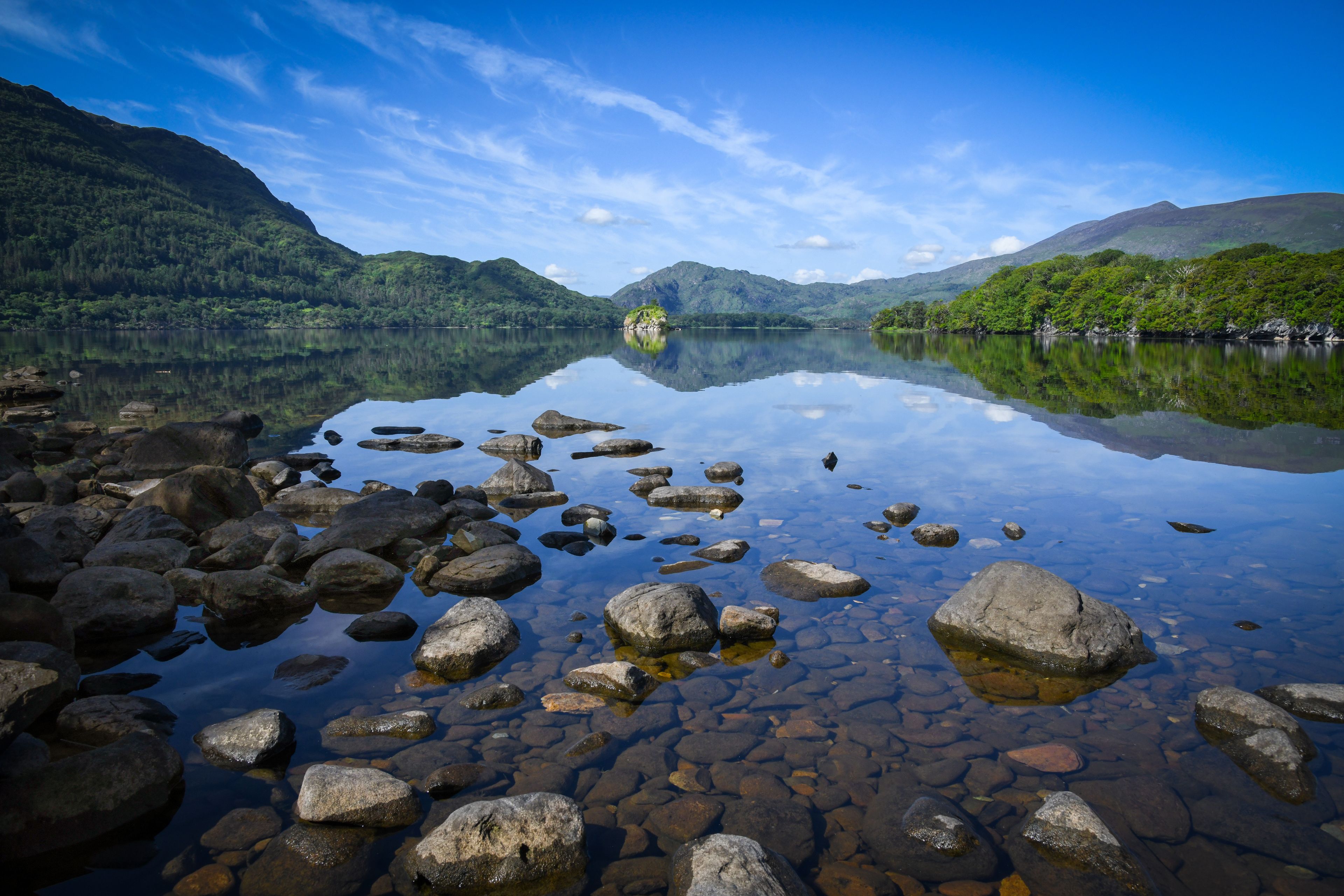 A calm lake with clear reflections of the surrounding mountains and sky.