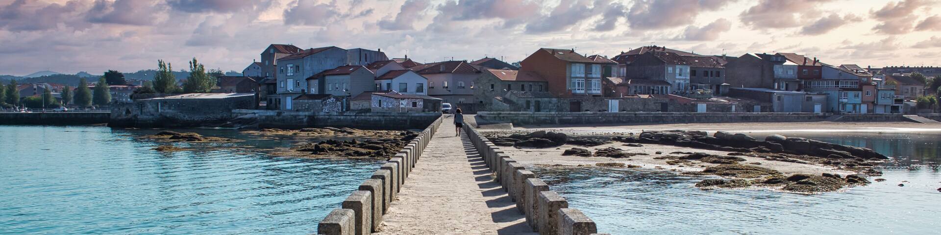 A stone pier leading to a coastal town with houses and a clear sky.