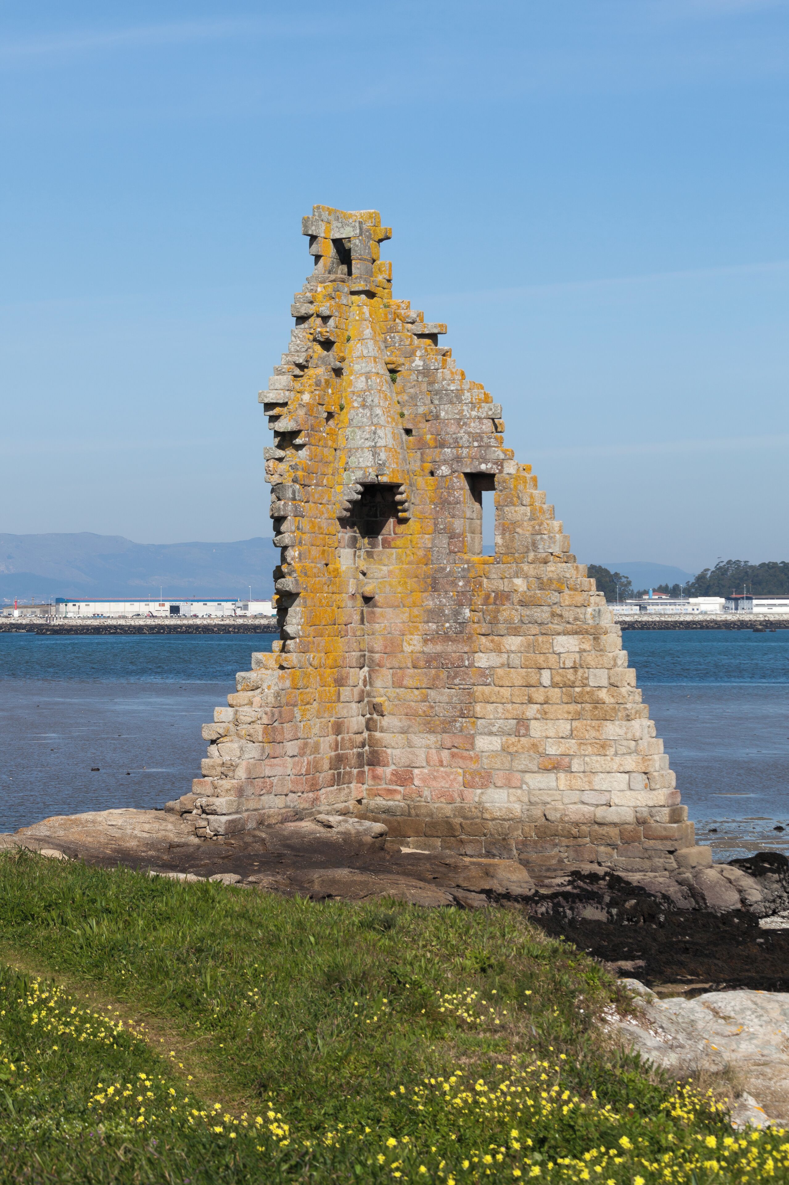 A weathered stone structure by the water with a clear sky.