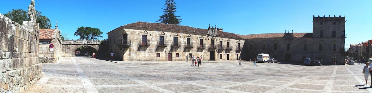 Un bâtiment historique en pierre, doté d’une tour, d’un pont de pierre et d’une place pavée.