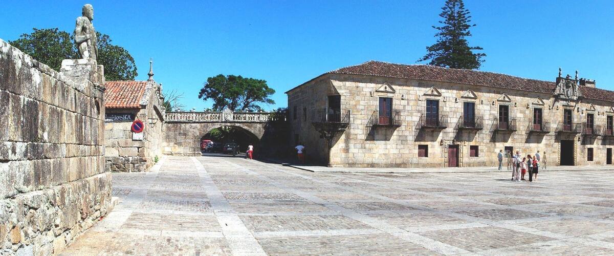 A historic stone building with a tower, a stone bridge, and a paved square.