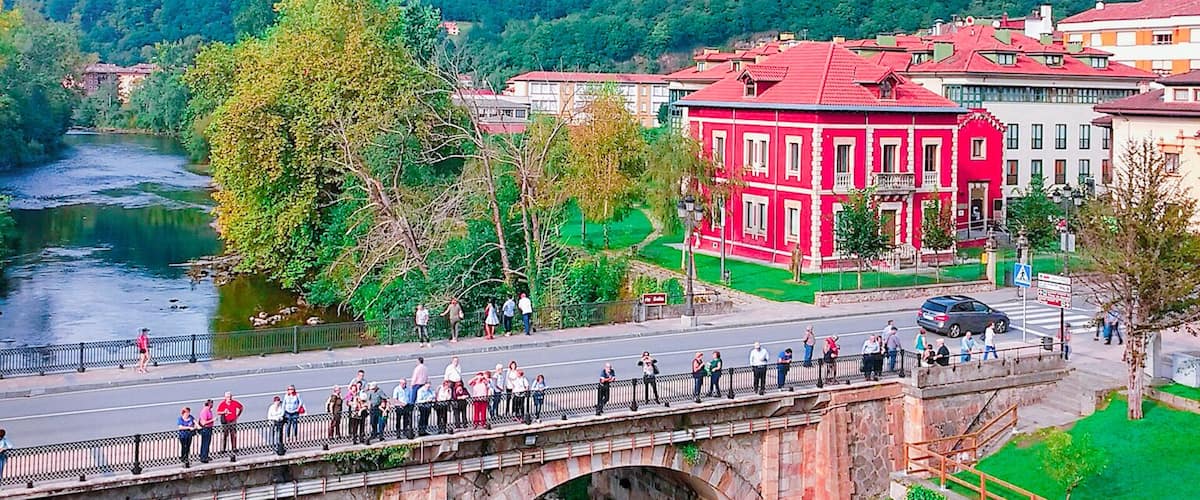 A stone bridge over a river, a red building, and green hills in the background.