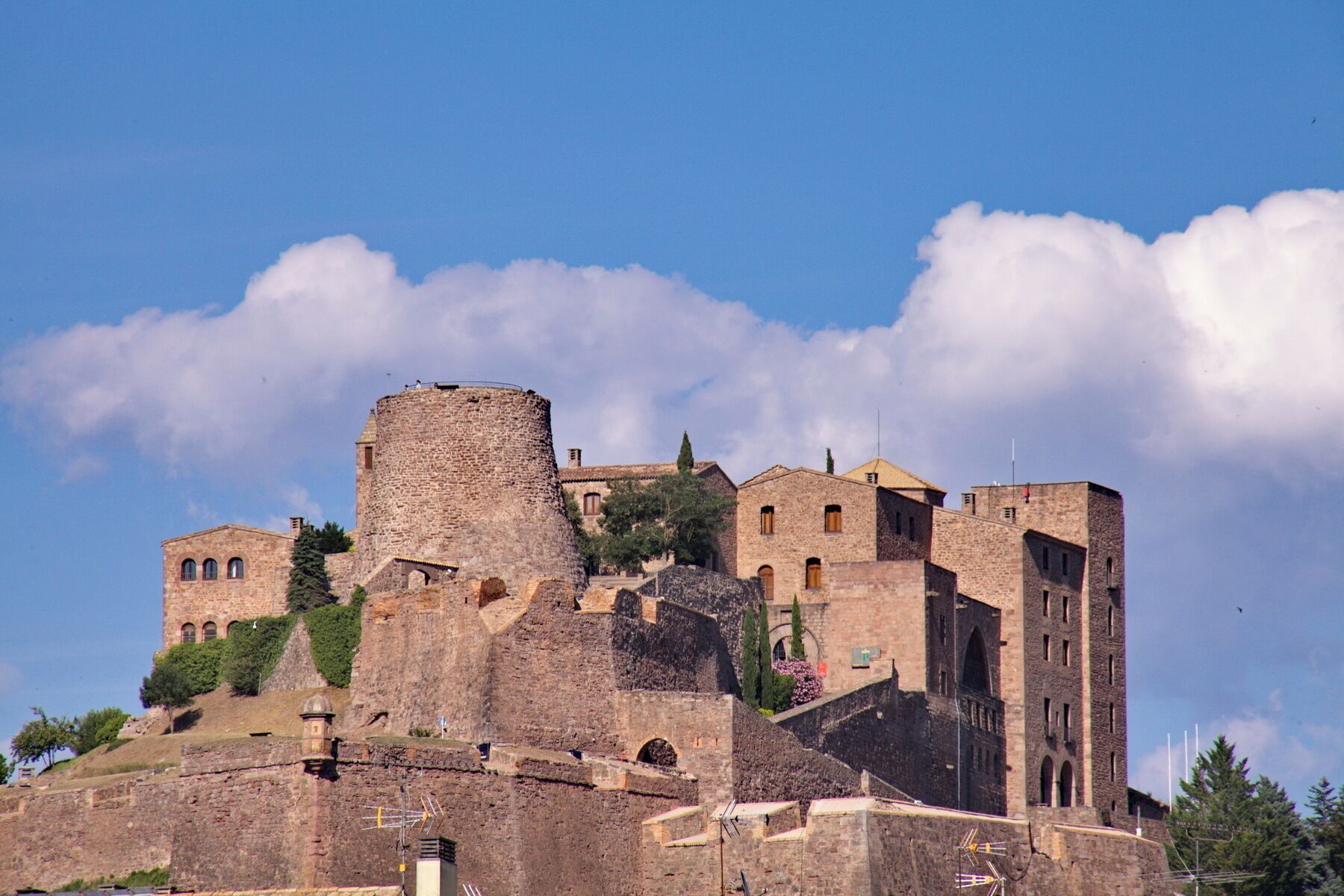 A historic stone castle with multiple towers and walls, set against a clear blue sky with clouds.