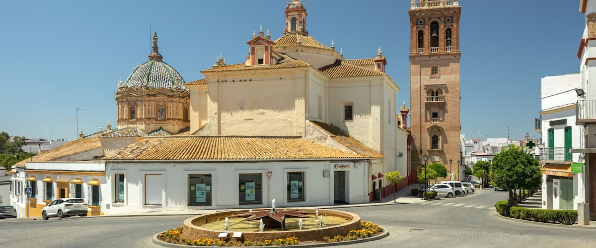 A historic church with a dome and bell tower, surrounded by a cobblestone square and modern buildings.